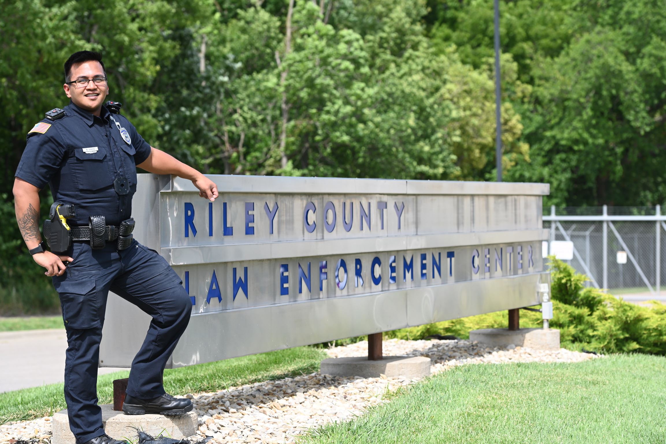 Police Officer Standing by the Riley County Law Enforcement Center Sign